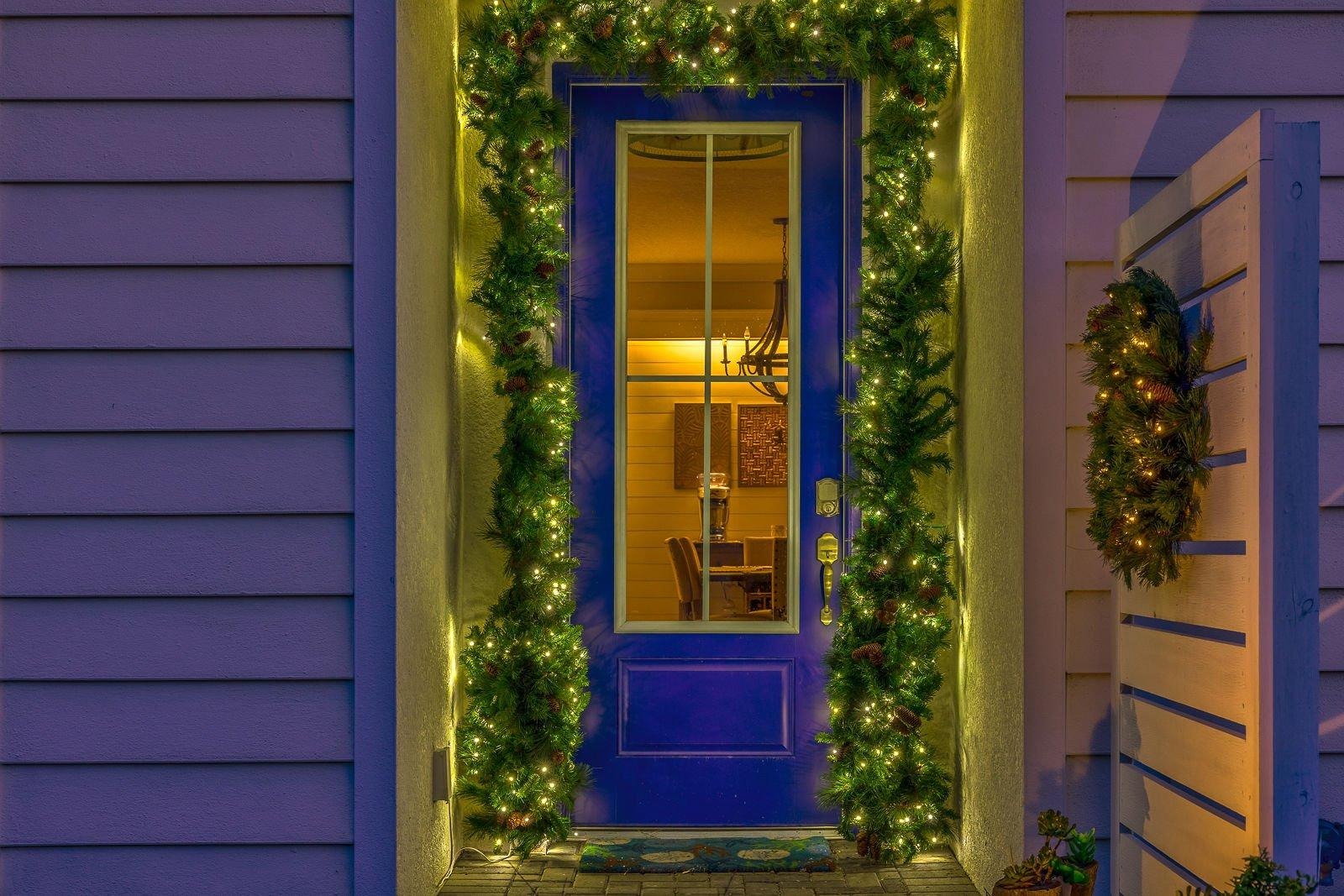 Front door framed in lit garland with a glowing wreath on a coastal Daytona home