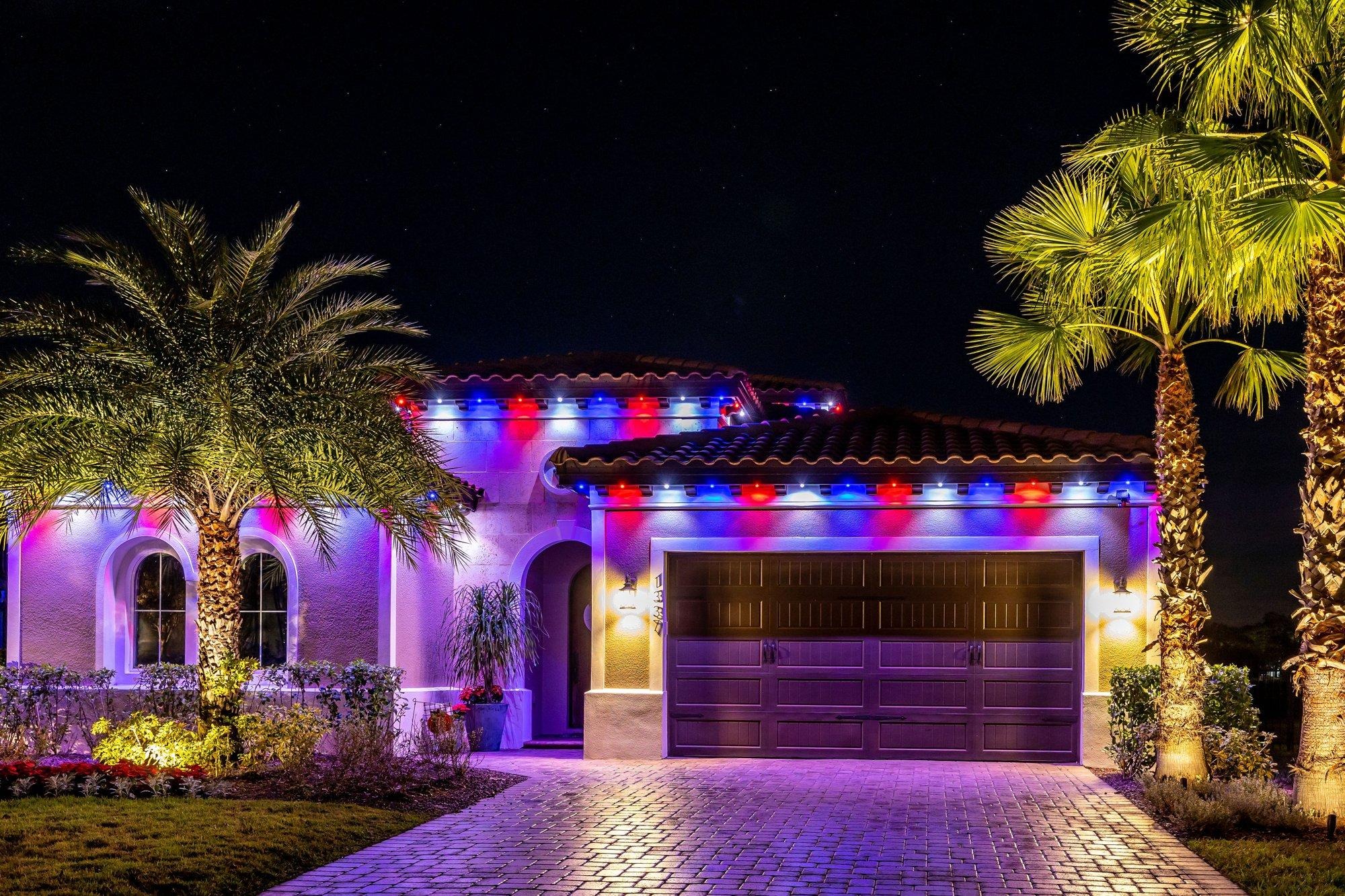 Florida home with permanent roofline lighting in red, white, and blue framed by illuminated palms