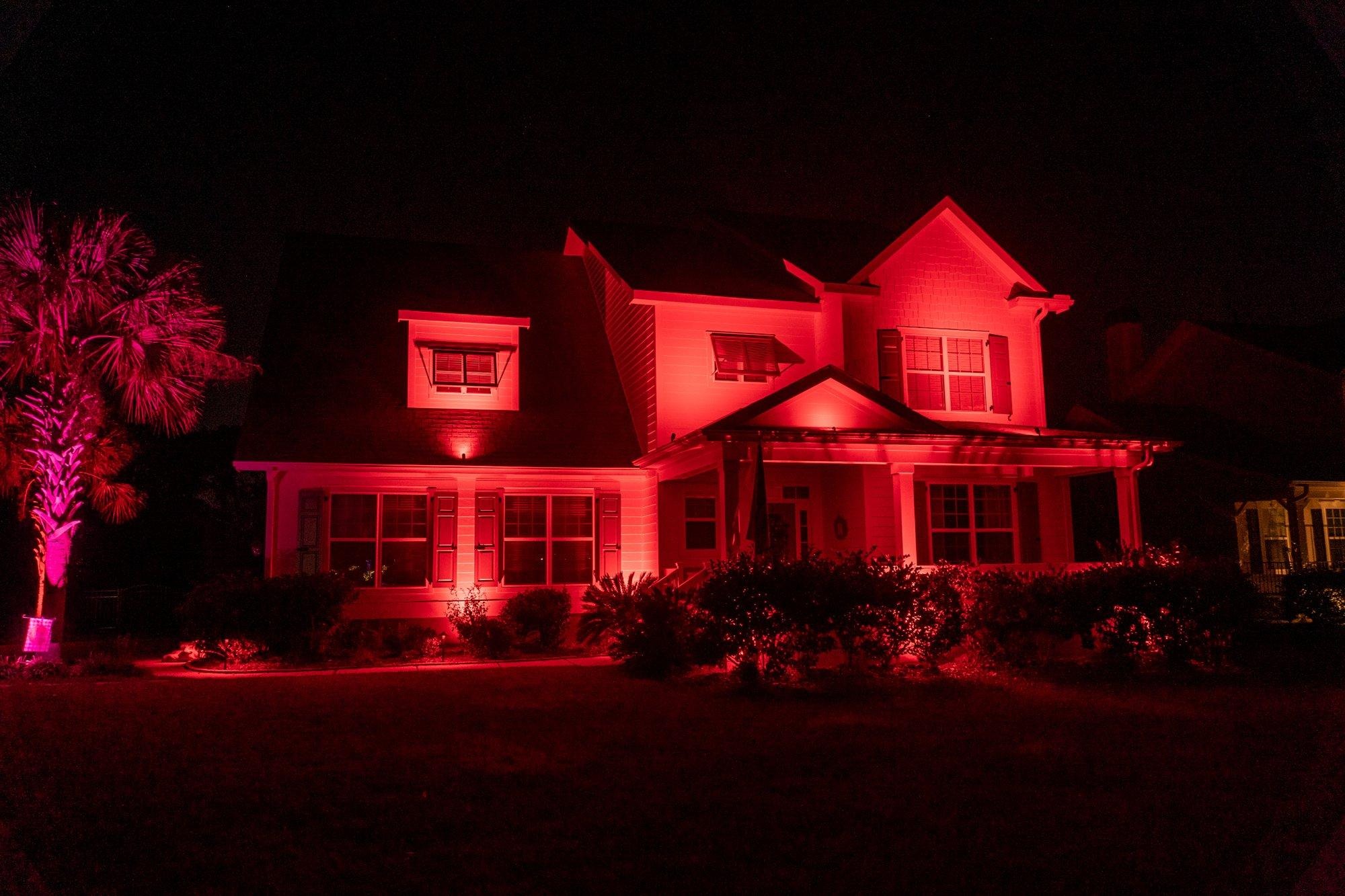 Coastal home washed entirely in festive red light from color-changing fixtures, with a palmetto glowing pink