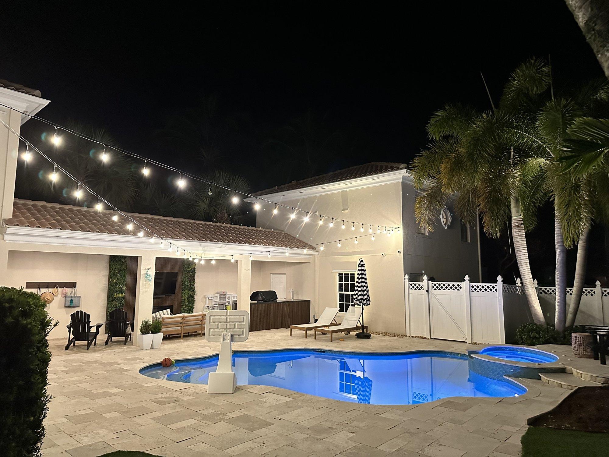 Festive string lights glowing above a pool deck and covered patio at a West Palm Beach home