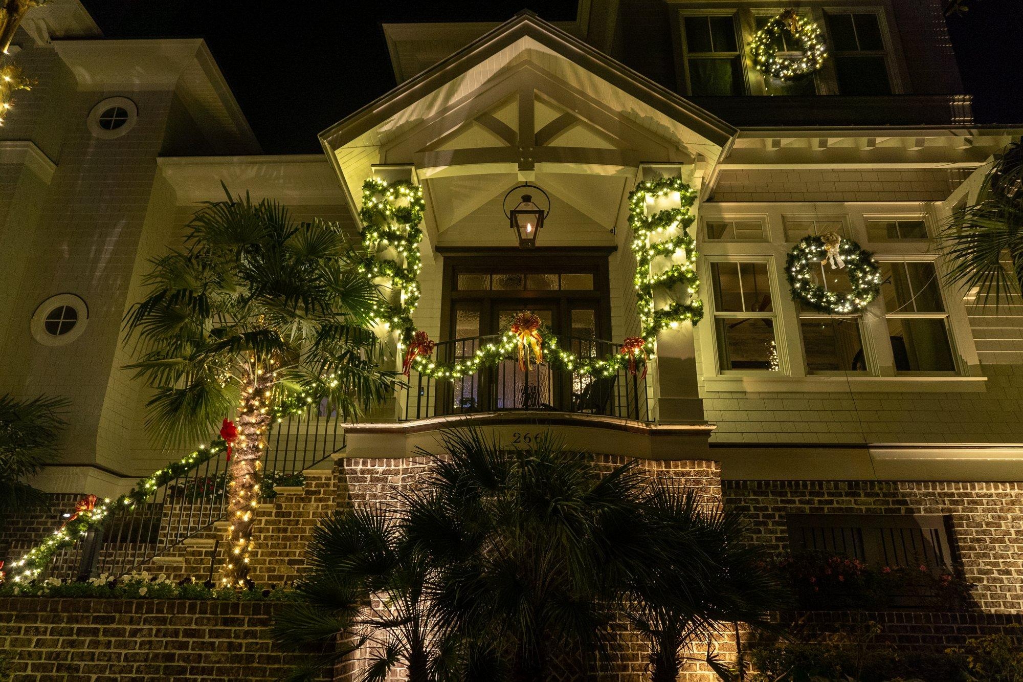 Lowcountry-style entry with lit garland, wreaths, and wrapped palmettos framing the front steps
