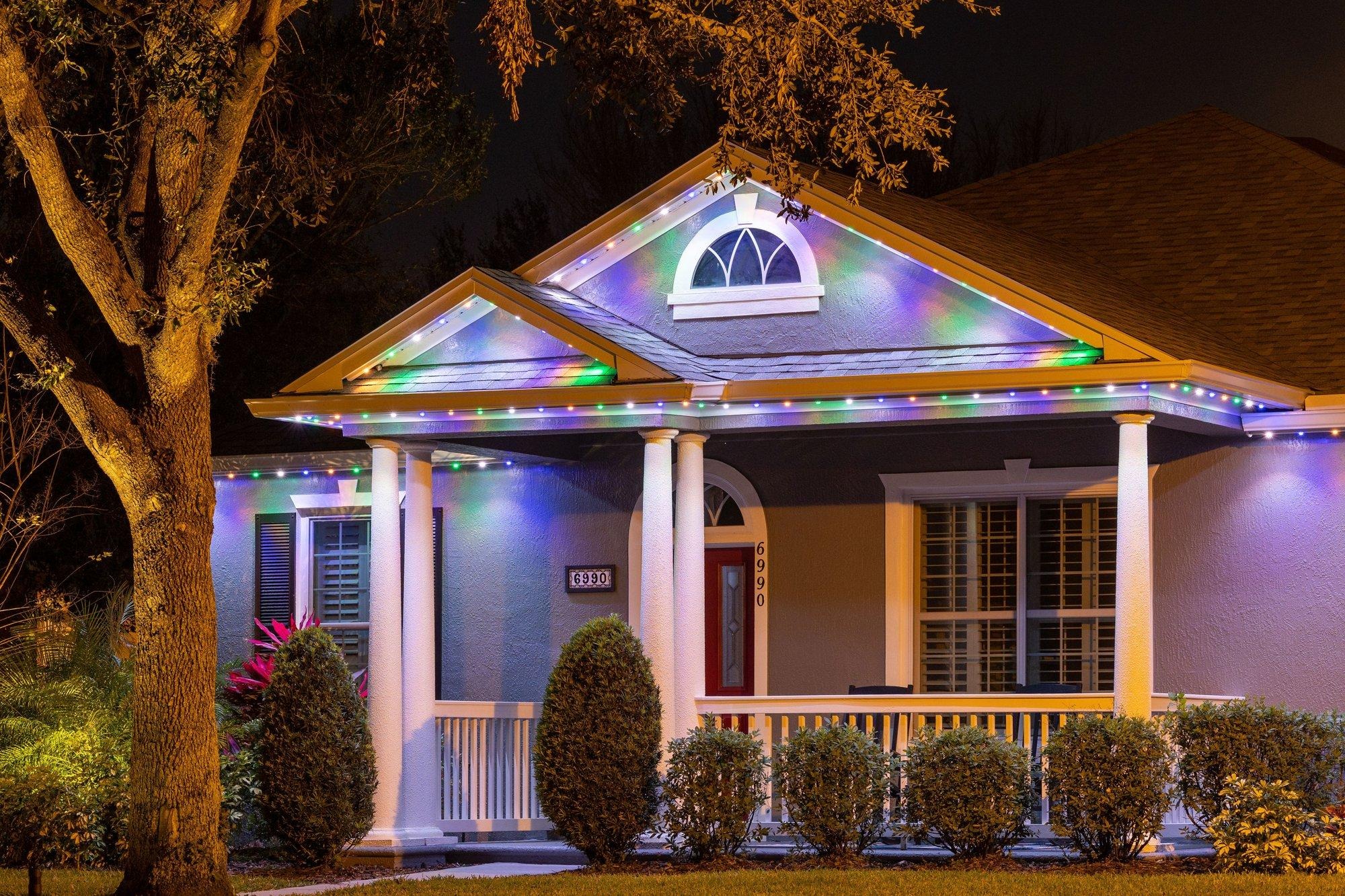 Permanent roofline lighting glowing in a multicolor holiday palette on a Florida home with a front porch
