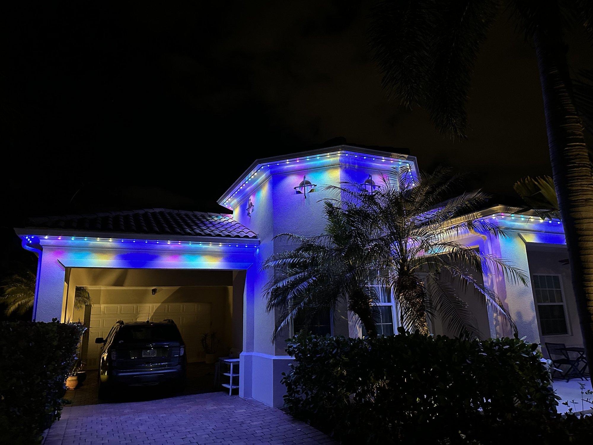 Permanent roofline lighting glowing in a rich multicolor palette on a West Palm Beach home with palms