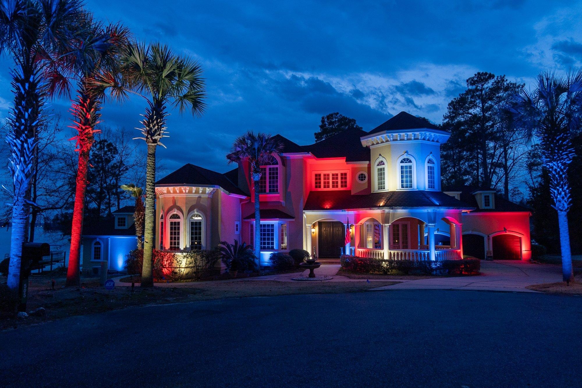 Grand Columbia-area estate lit in red, white, and blue with palms washed in patriotic color