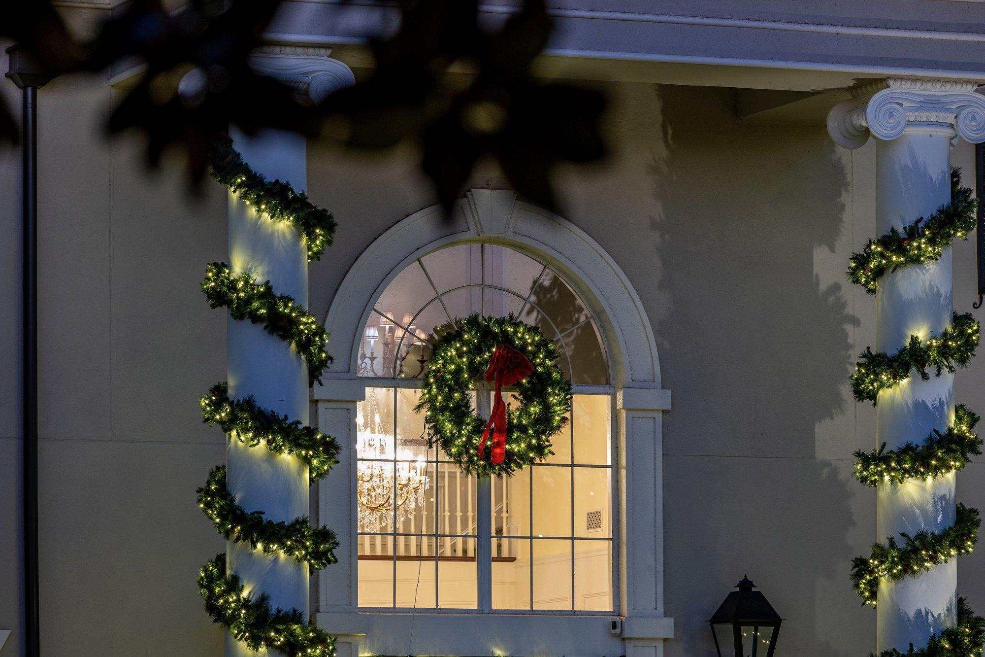 Columns wrapped in lit garland and a glowing wreath centered in an arched window