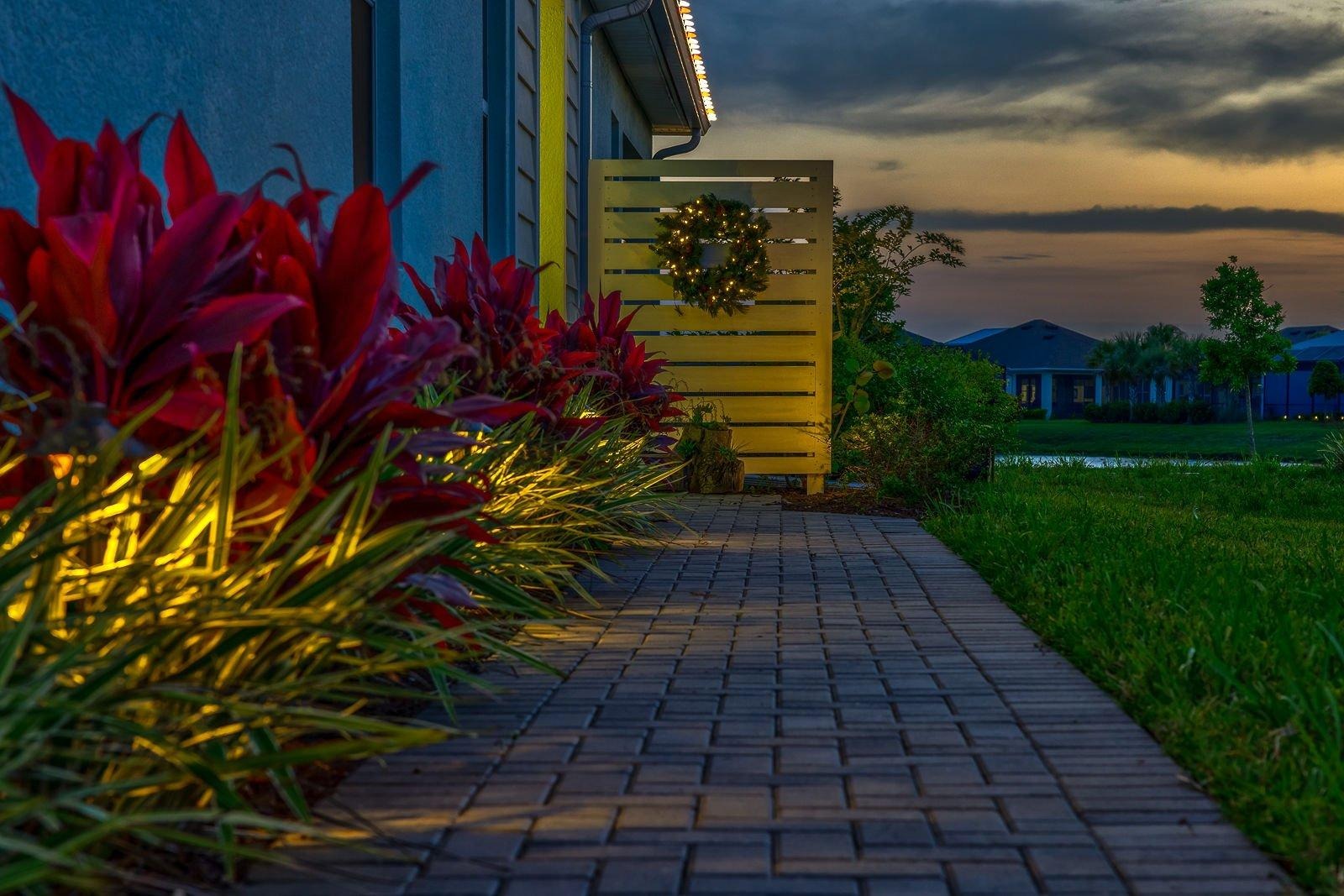 Sunset walkway lined with glowing landscape lighting and a holiday wreath on a coastal home