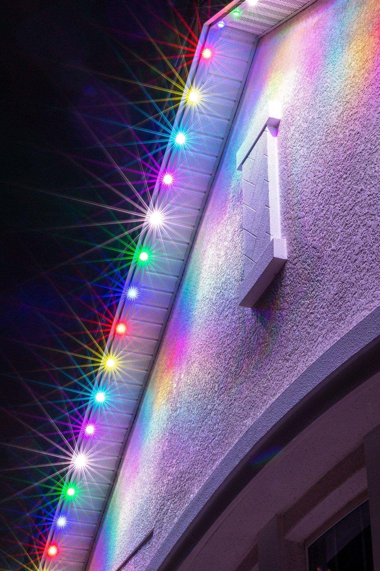 Close-up of permanent roofline lighting glowing in a multicolor pattern along a home’s eave