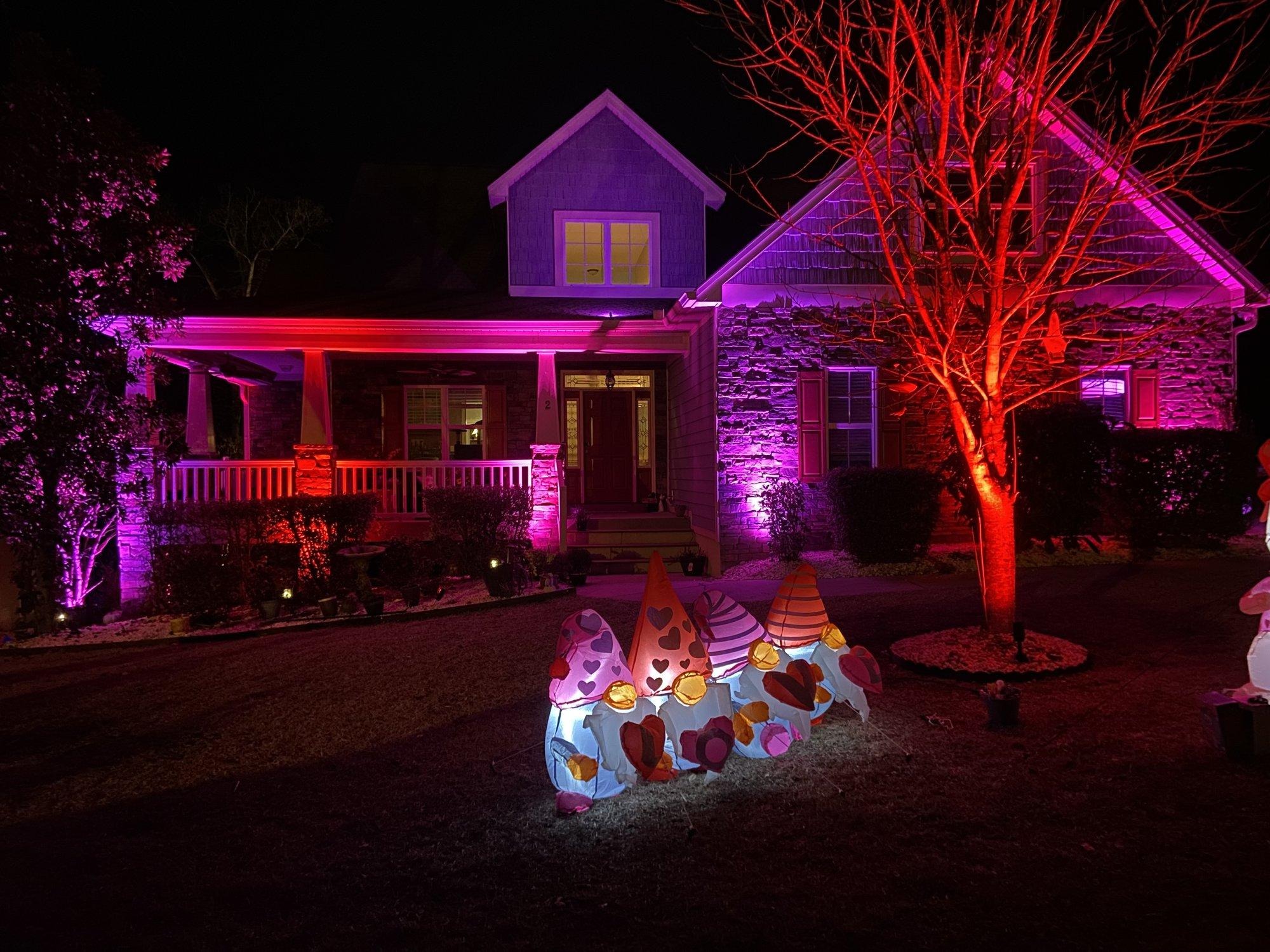 Brick home washed in pink, red, and purple light from color-changing fixtures for Valentine’s Day