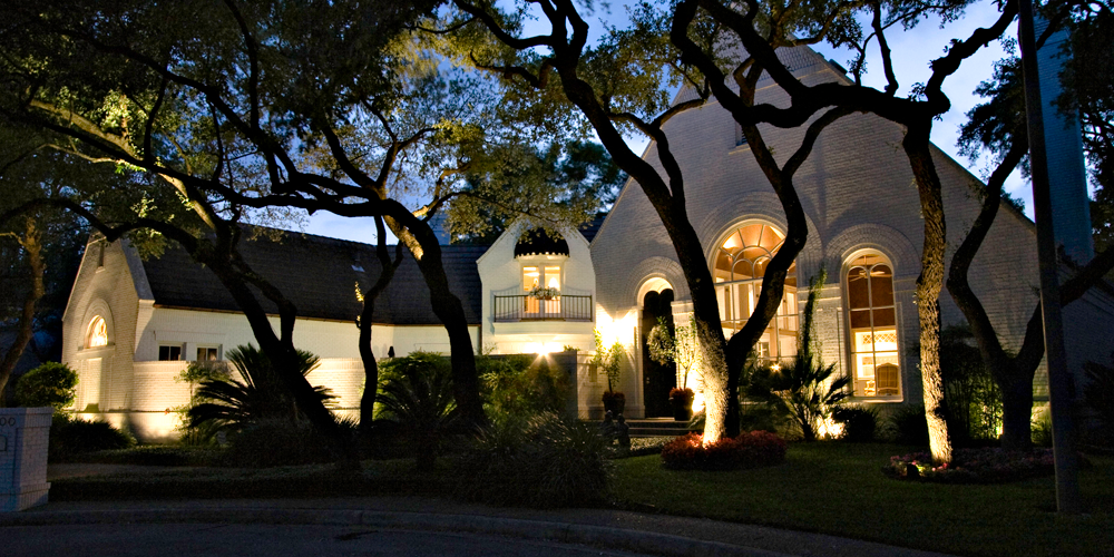 Architectural home with lighting and trees