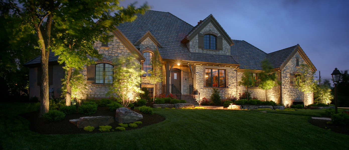 architectural lighting on front a stone house as well as some lit trees