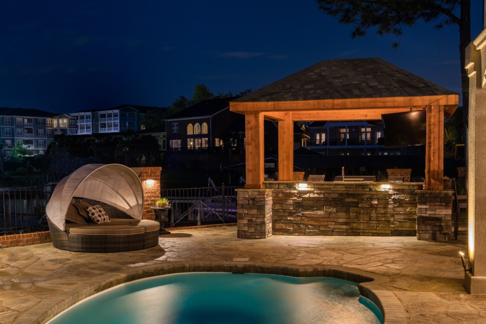 pool with lounge couch and gazebo in backyard that is illuminated with led lighting at night time