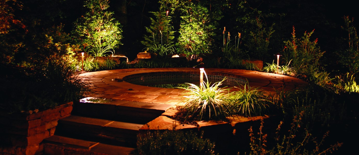 A circular stone patio with a fountain and trees at night

Description automatically generated