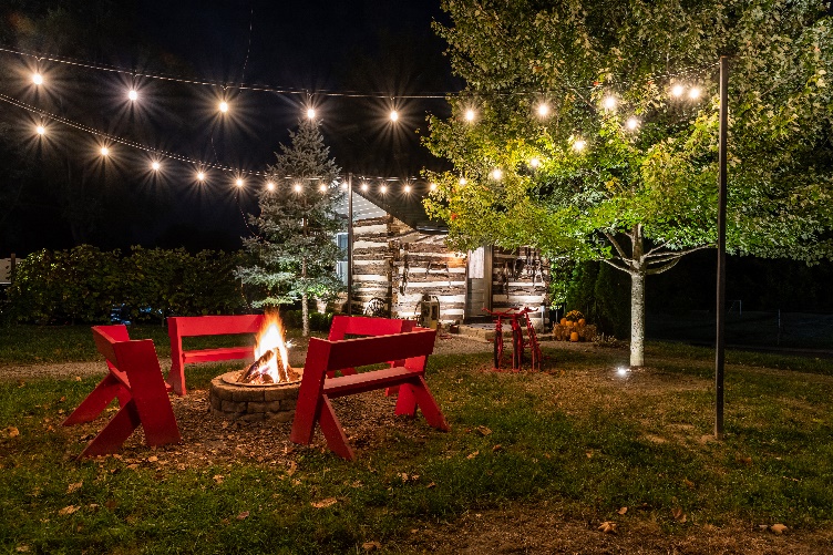 A fire pit in a yard with a log cabin and trees