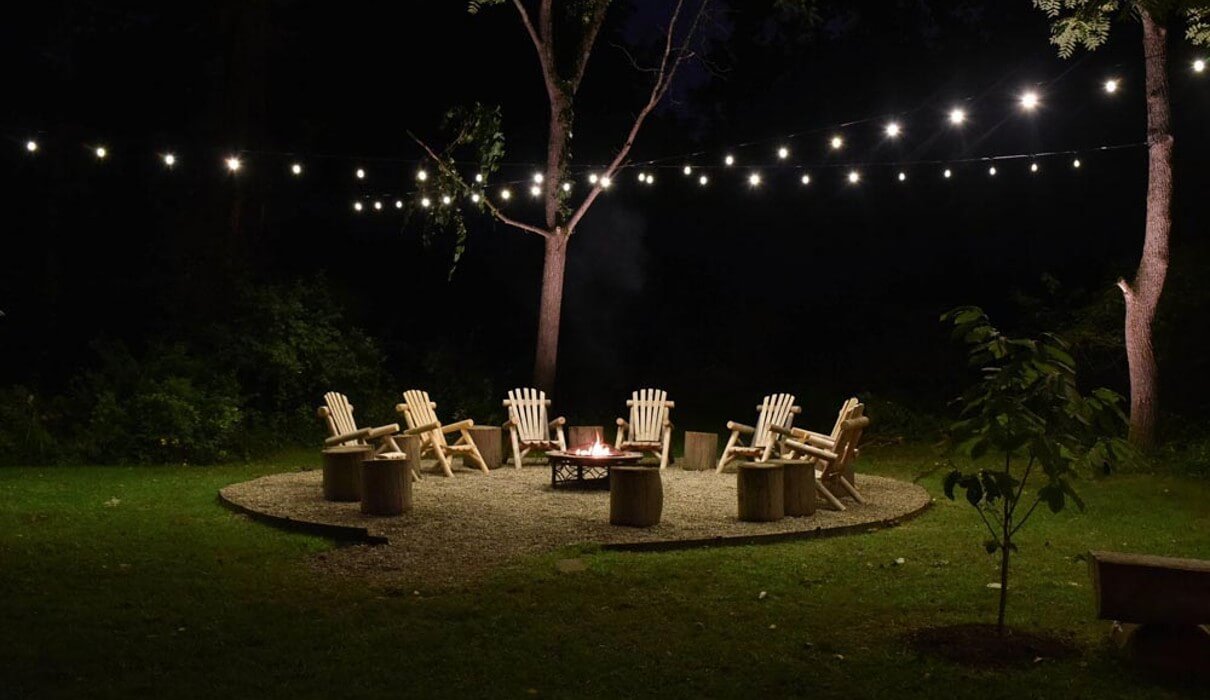Adirondack chairs around a firepit and under string lighting