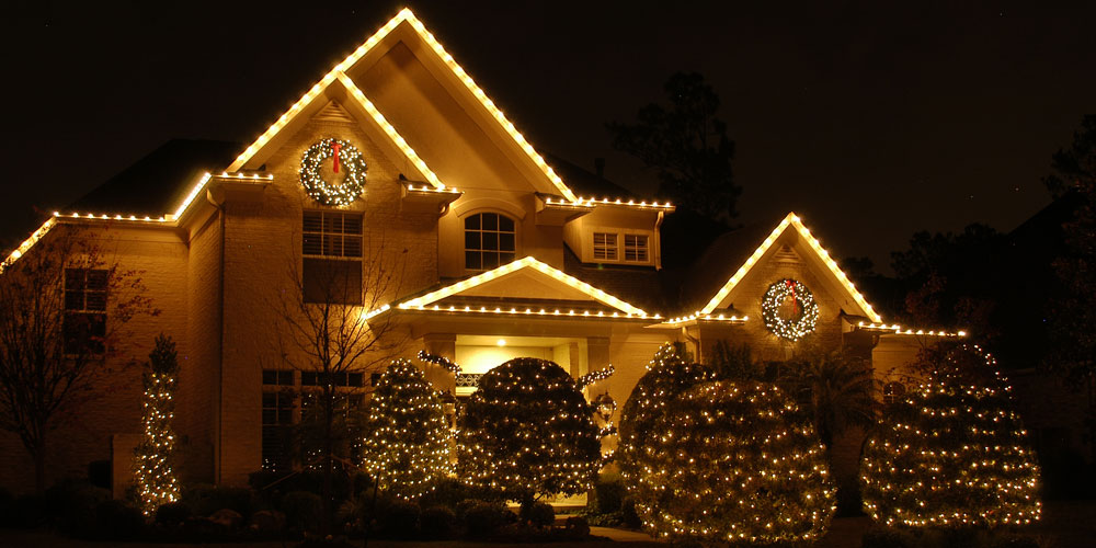 Home with holiday lighting on it and the surrounding trees